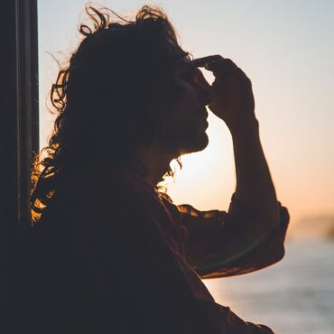 man holding forehead under sunset