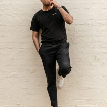 man in black crew neck t-shirt and blue denim jeans leaning on white wall